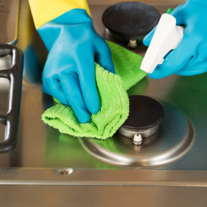 Gloved Hands Cleaning Stove Top Range with Spray bottle and Microfiber Rag. Closeup horizontal image of hands wearing rubber gloves while cleaning stove top range with spray bottle and microfiber rag