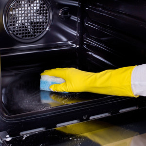 Woman cleaning oven. Close up of female hand with yellow protective gloves cleaning oven
