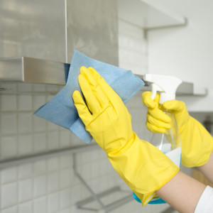 Closeup of female hands in gloves cleaning the extractor hood. Close up of female hands in rubber protective yellow gloves cleaning the kitchen metal extractor hood with rag and spray bottle detergent. Home, housekeeping concept